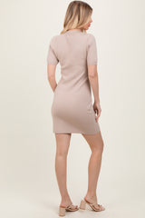 woman wearing a fitted beige short sleeve dress, styled with heels, viewed from the back on a neutral background