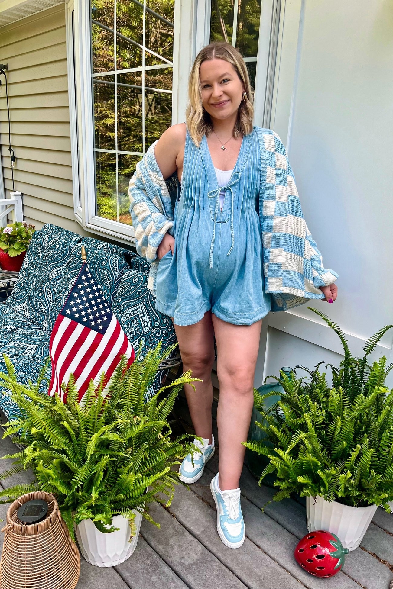 woman wearing a light blue maternity romper with a cozy cardigan, showing off her baby bump while standing outdoors