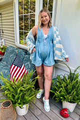 woman wearing a light blue maternity romper with a cozy cardigan, showing off her baby bump while standing outdoors