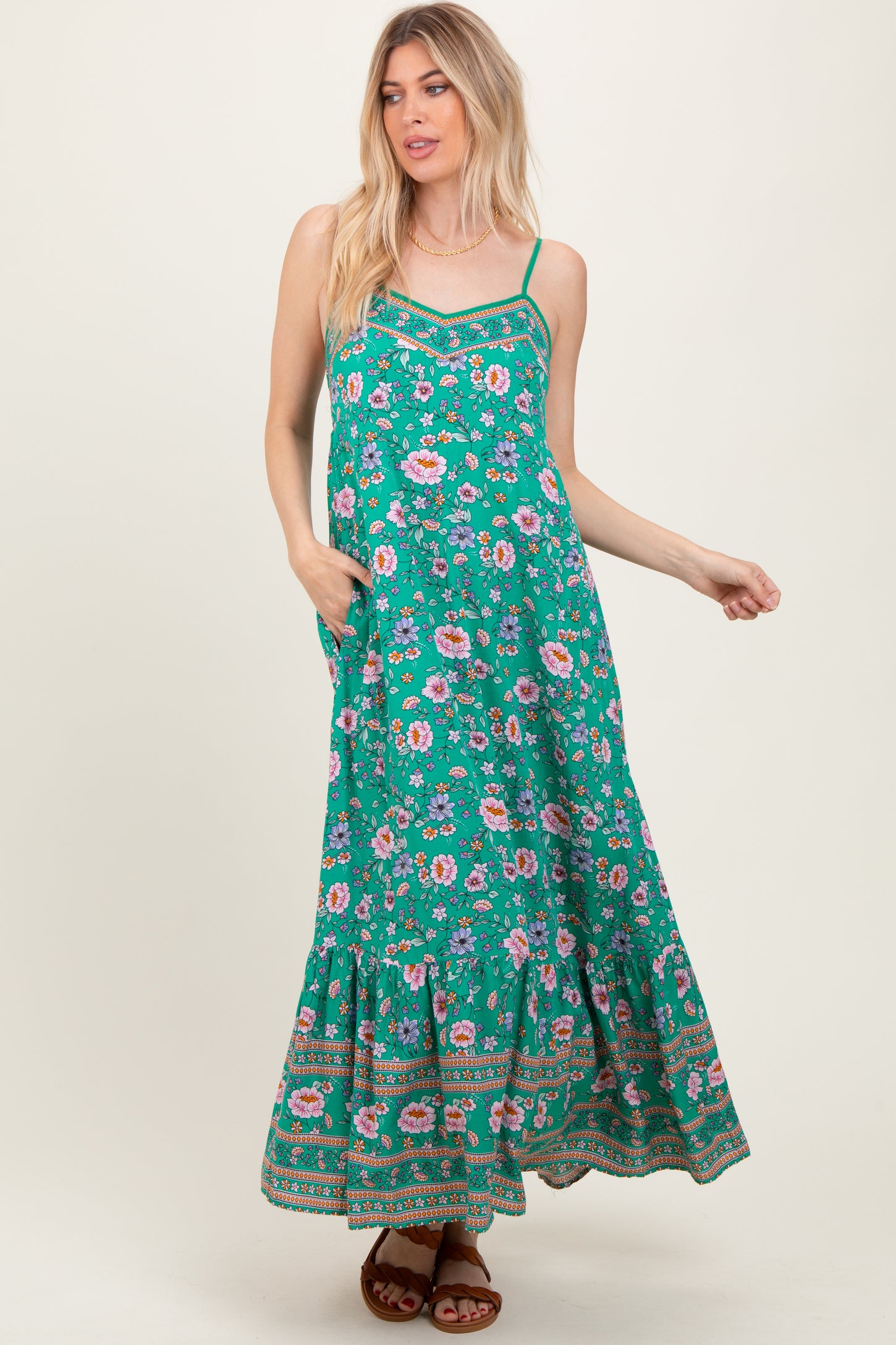 woman wearing a green maxi dress with floral print and spaghetti straps, featuring a tiered hem and pockets