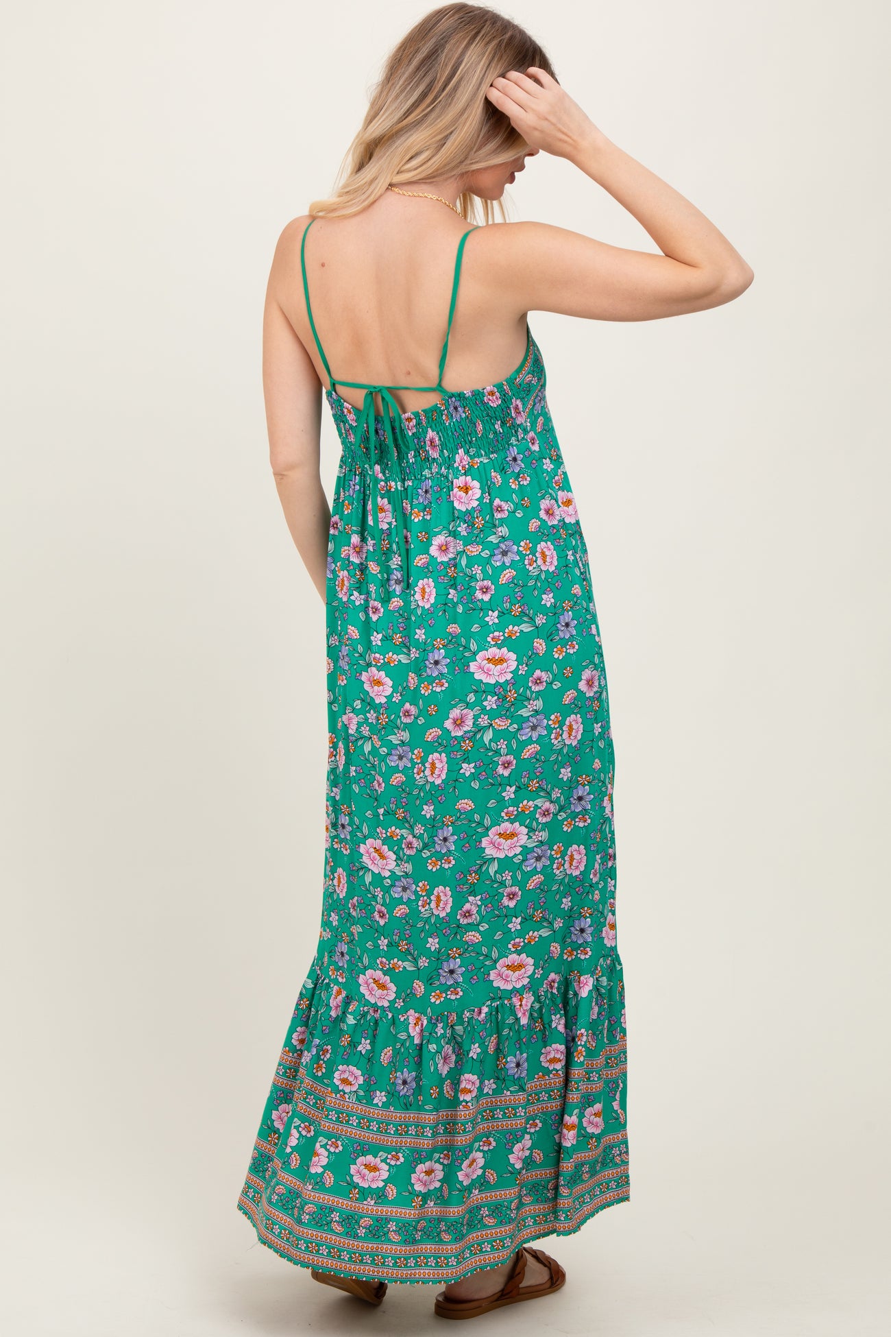 woman wearing a green floral maxi dress with a tiered skirt and spaghetti straps, showing the back view