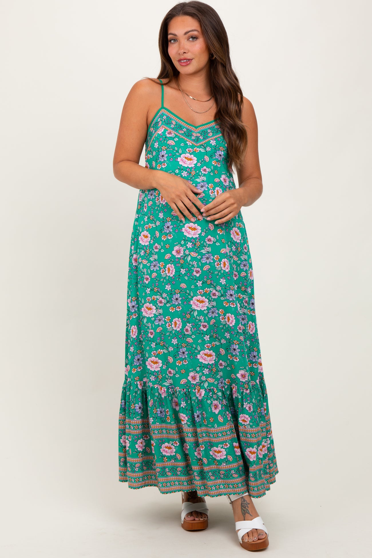 woman wearing a green floral maternity maxi dress with adjustable straps and a tiered skirt, showing a baby bump