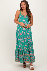 woman wearing a green floral maternity maxi dress with adjustable straps and a tiered skirt, showing a baby bump