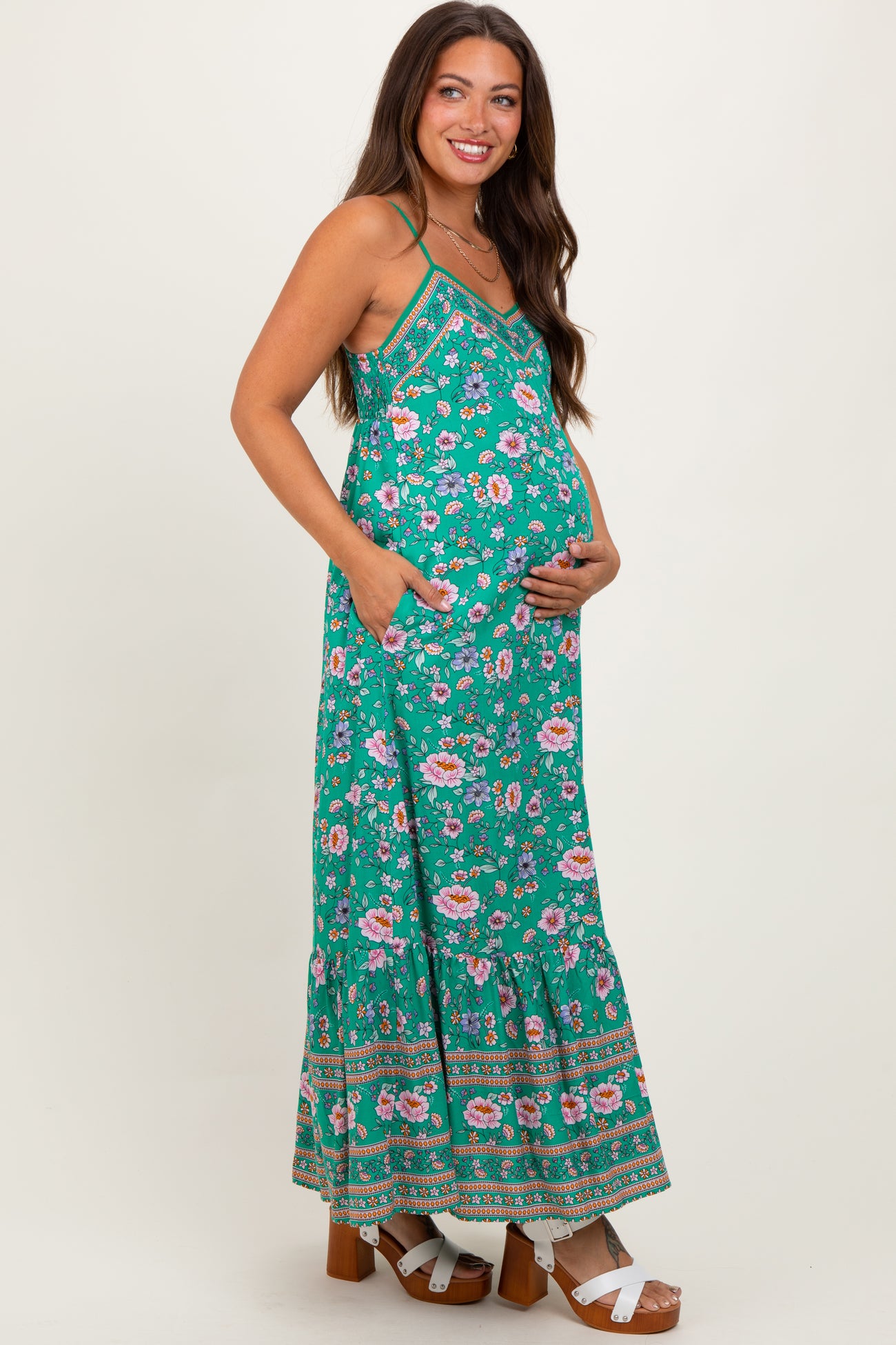 woman wearing a green floral maternity maxi dress and holding her baby bump
