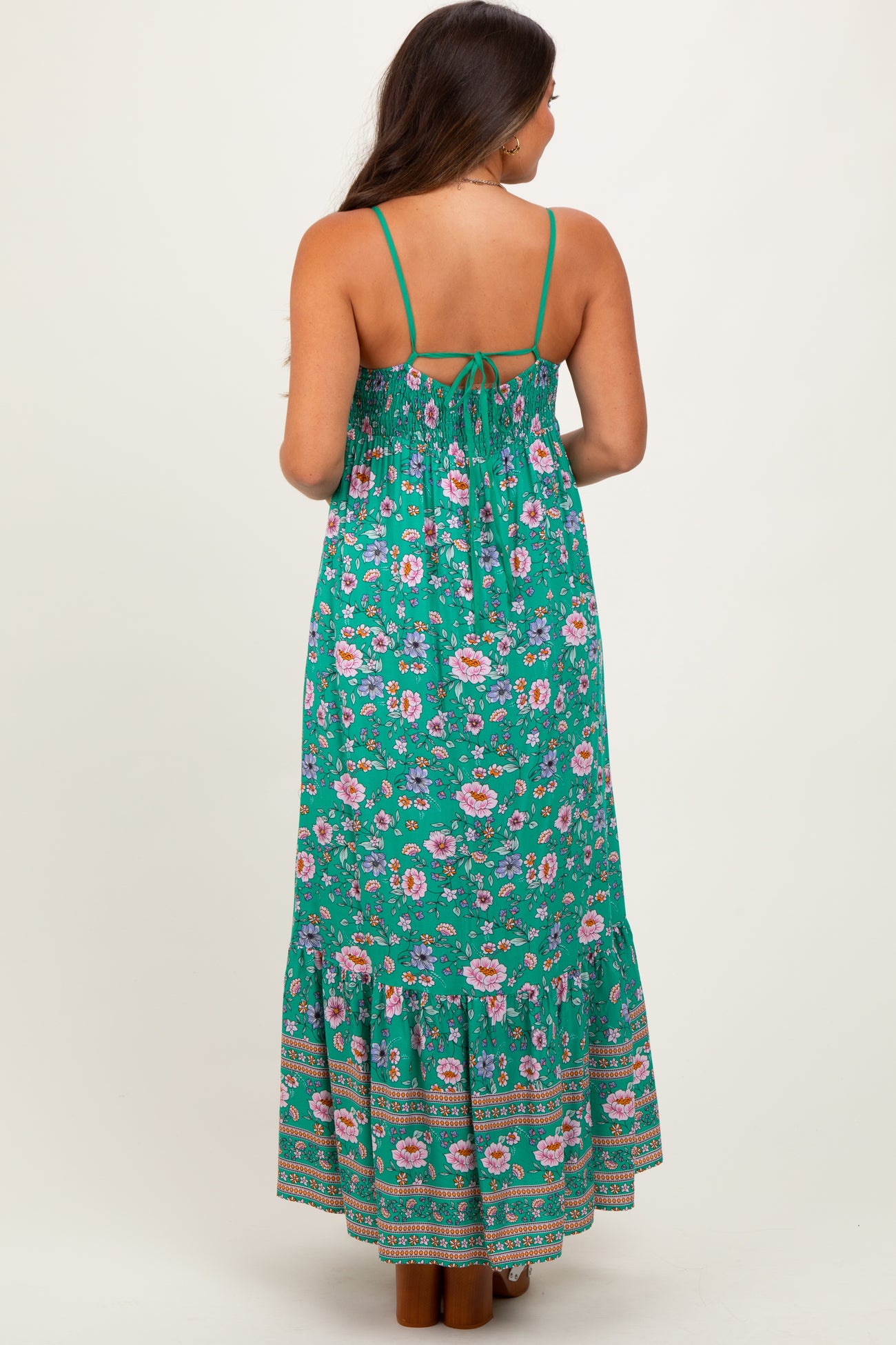 woman wearing a green floral maternity maxi dress with a tie-back and tiered skirt, showing a baby bump from the back
