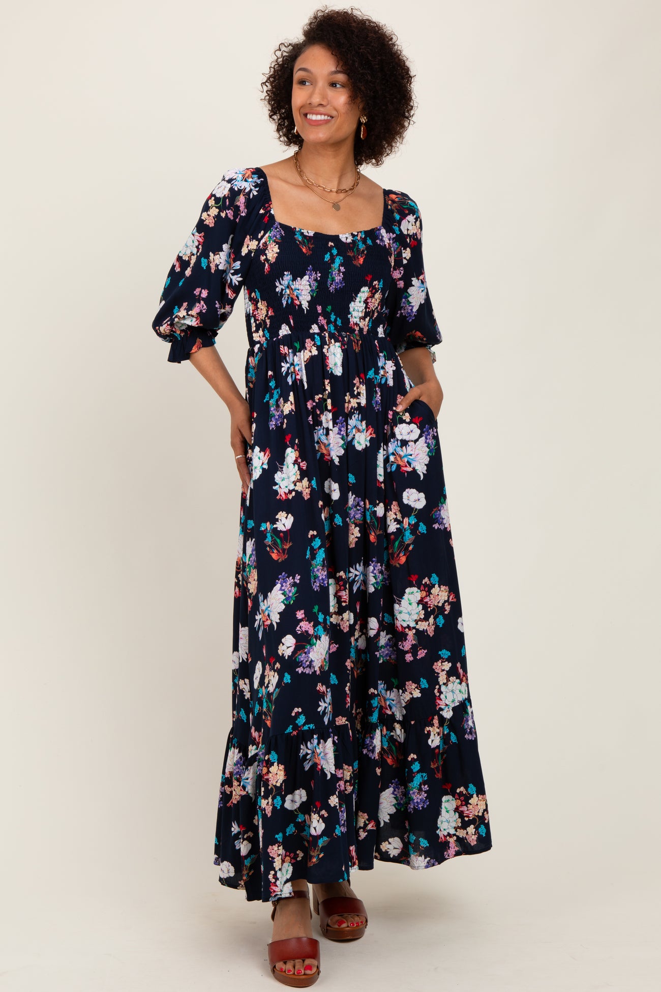 woman wearing a navy floral maxi dress with puff sleeves and pockets, smiling and posing against a neutral background