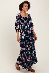 woman wearing a navy floral maxi dress with puff sleeves and a ruffled hem, standing and smiling