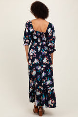 woman wearing a navy floral maxi dress with a ruffled neckline and open back, styled with brown heeled sandals
