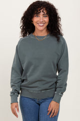 woman wearing a dark green long sleeve sweatshirt with a crew neckline and ribbed cuffs, smiling at the camera