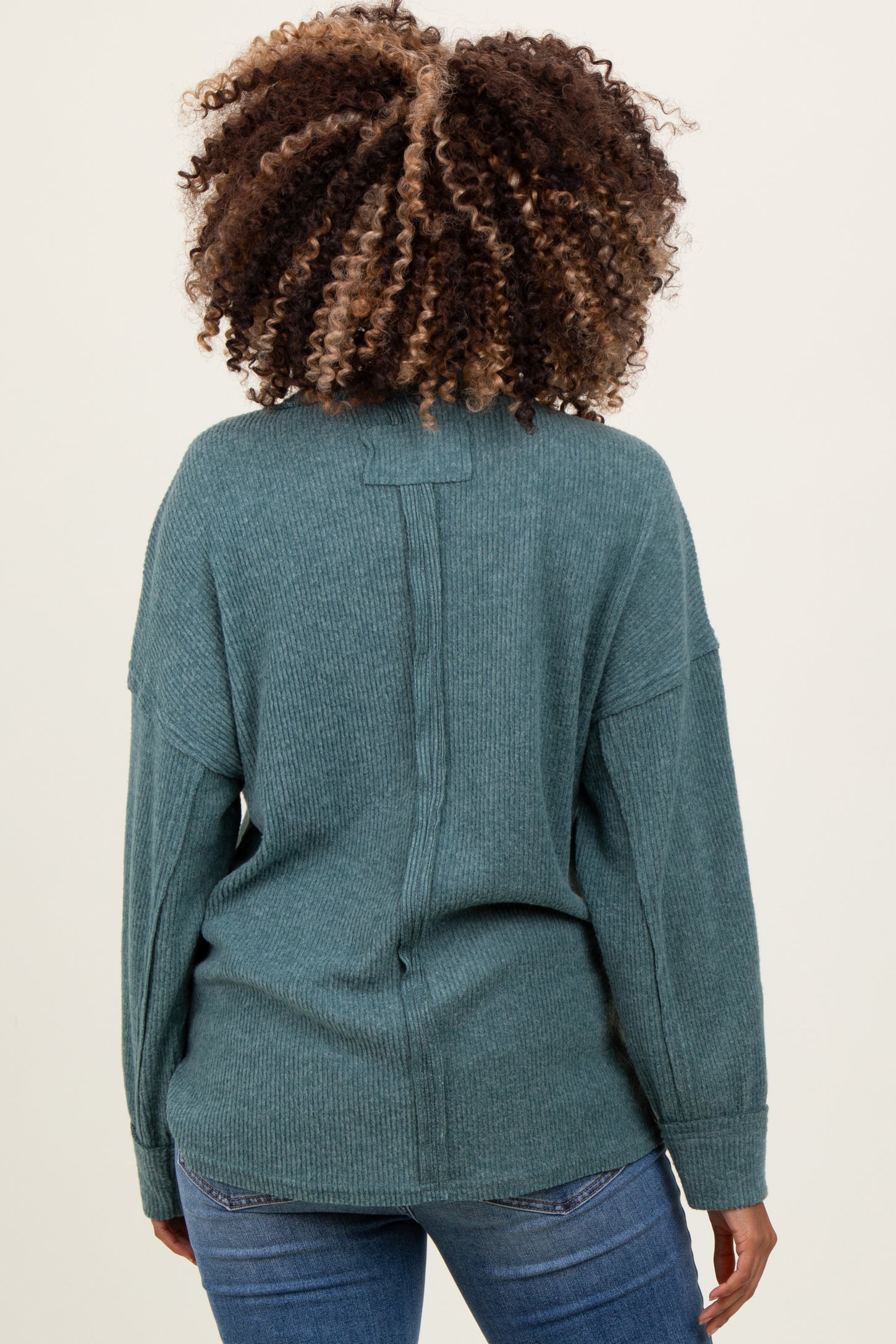 woman wearing a teal maternity sweater with a relaxed fit and back seam detail, styled with blue jeans