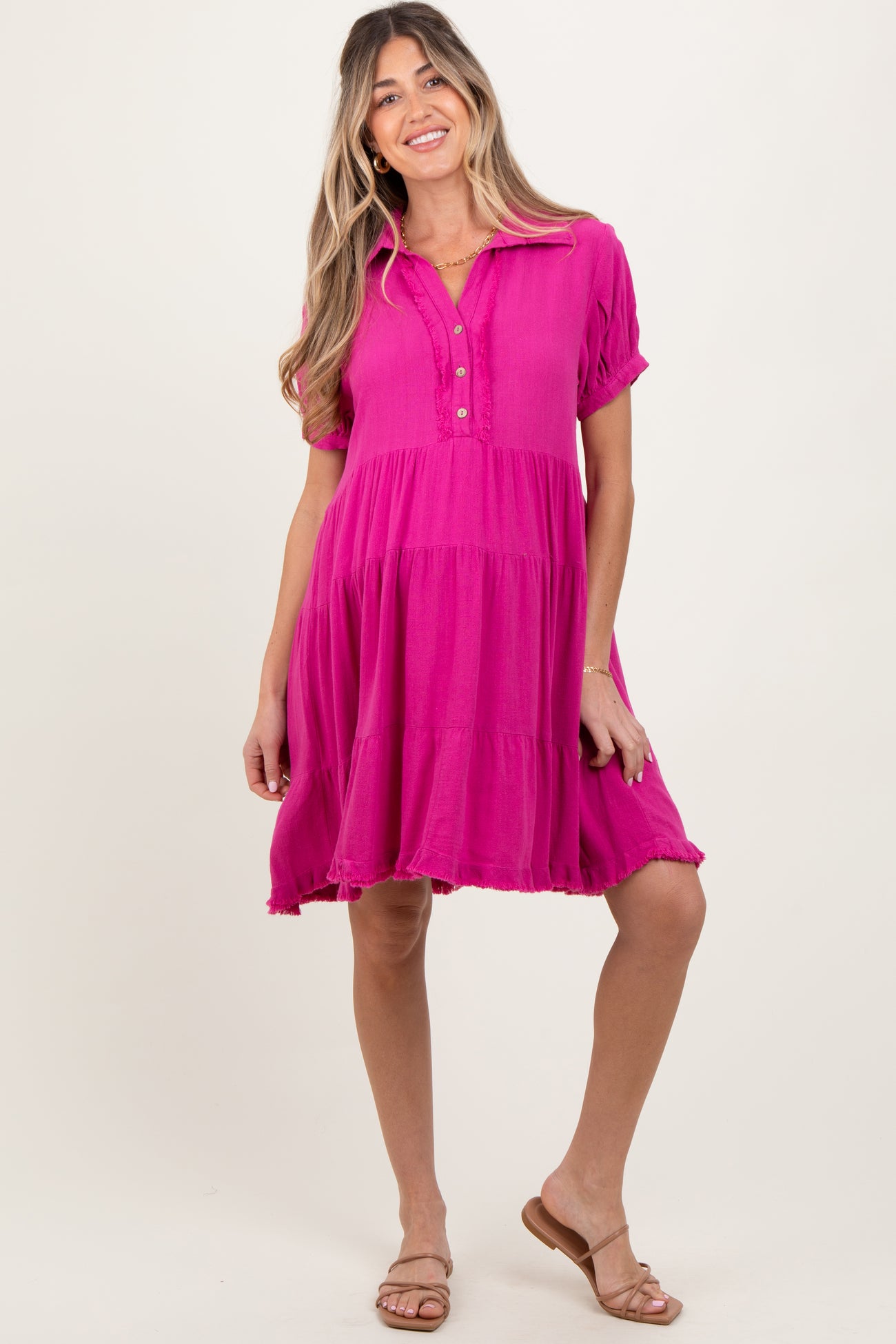 woman wearing a pink maternity dress with short sleeves and button details, standing and smiling