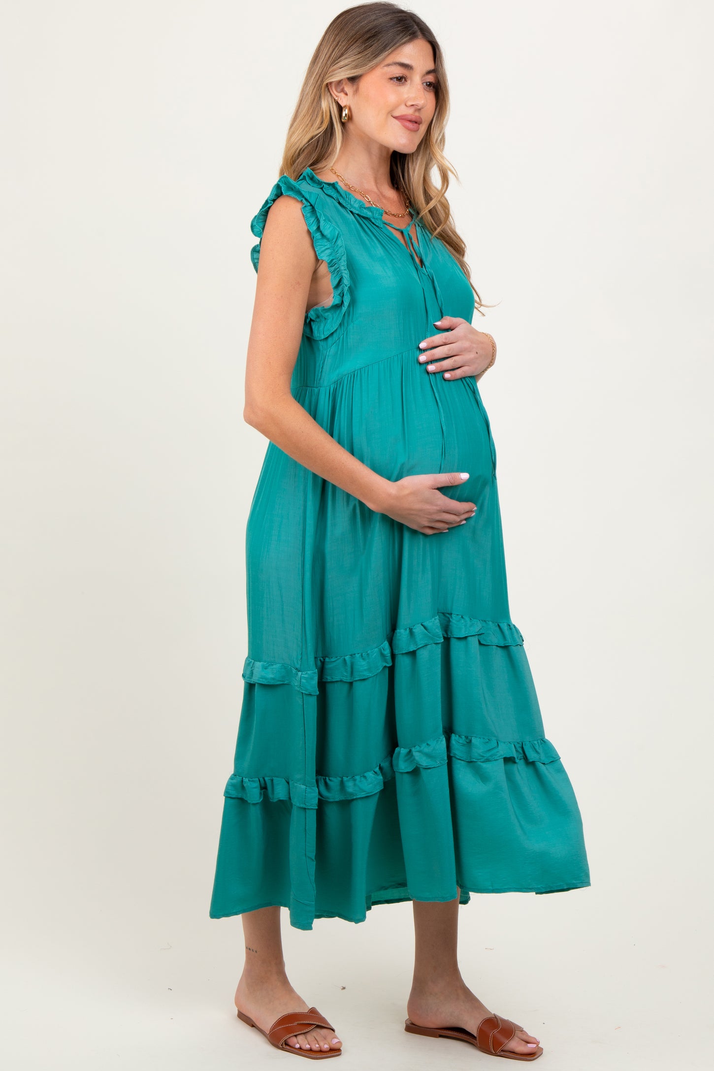 woman wearing a teal maternity dress with ruffles and tiered skirt, holding her baby bump