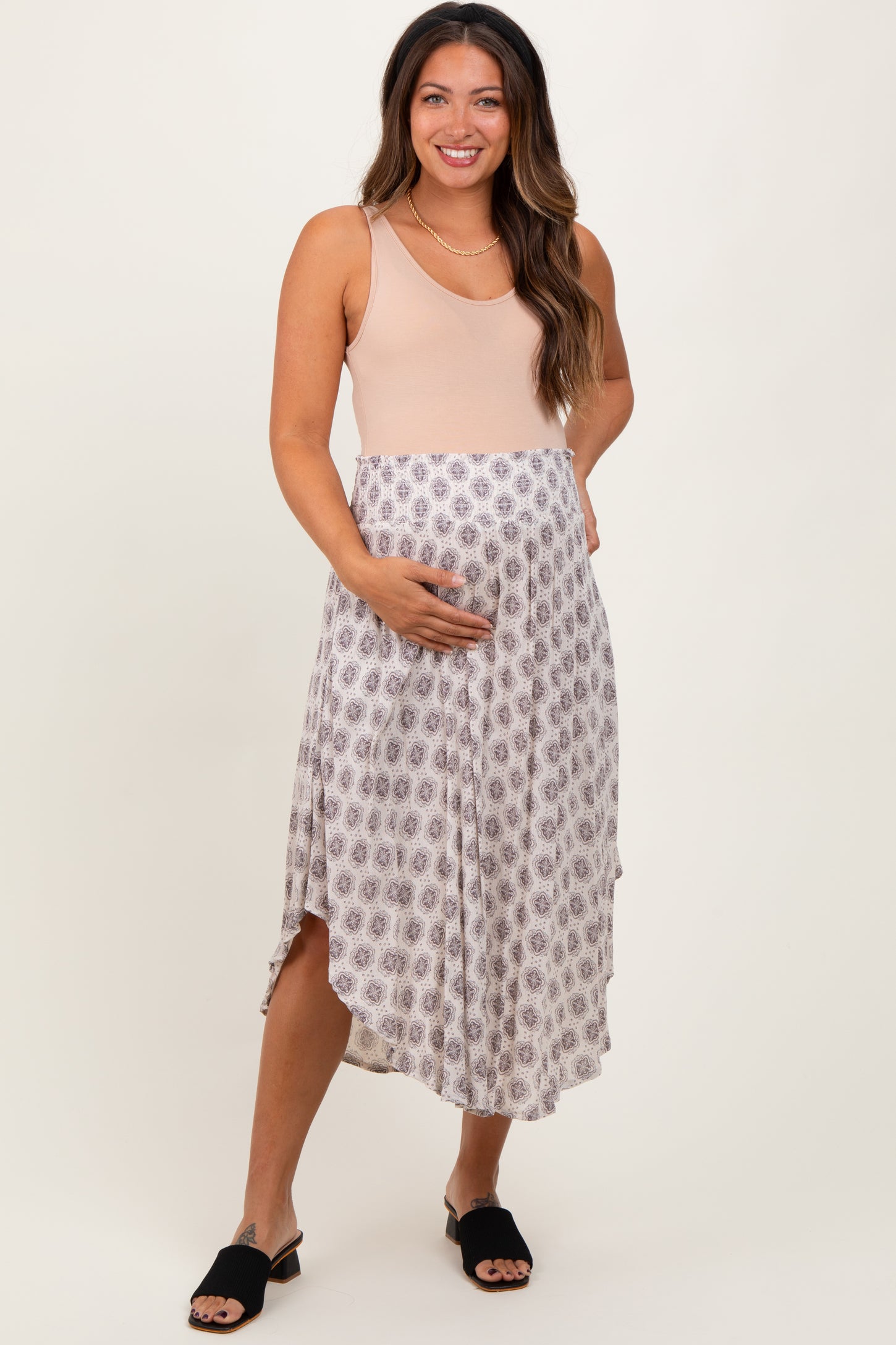 woman wearing a beige maternity dress with a printed skirt and holding her baby bump