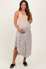 woman wearing a beige maternity dress with a printed skirt and holding her baby bump