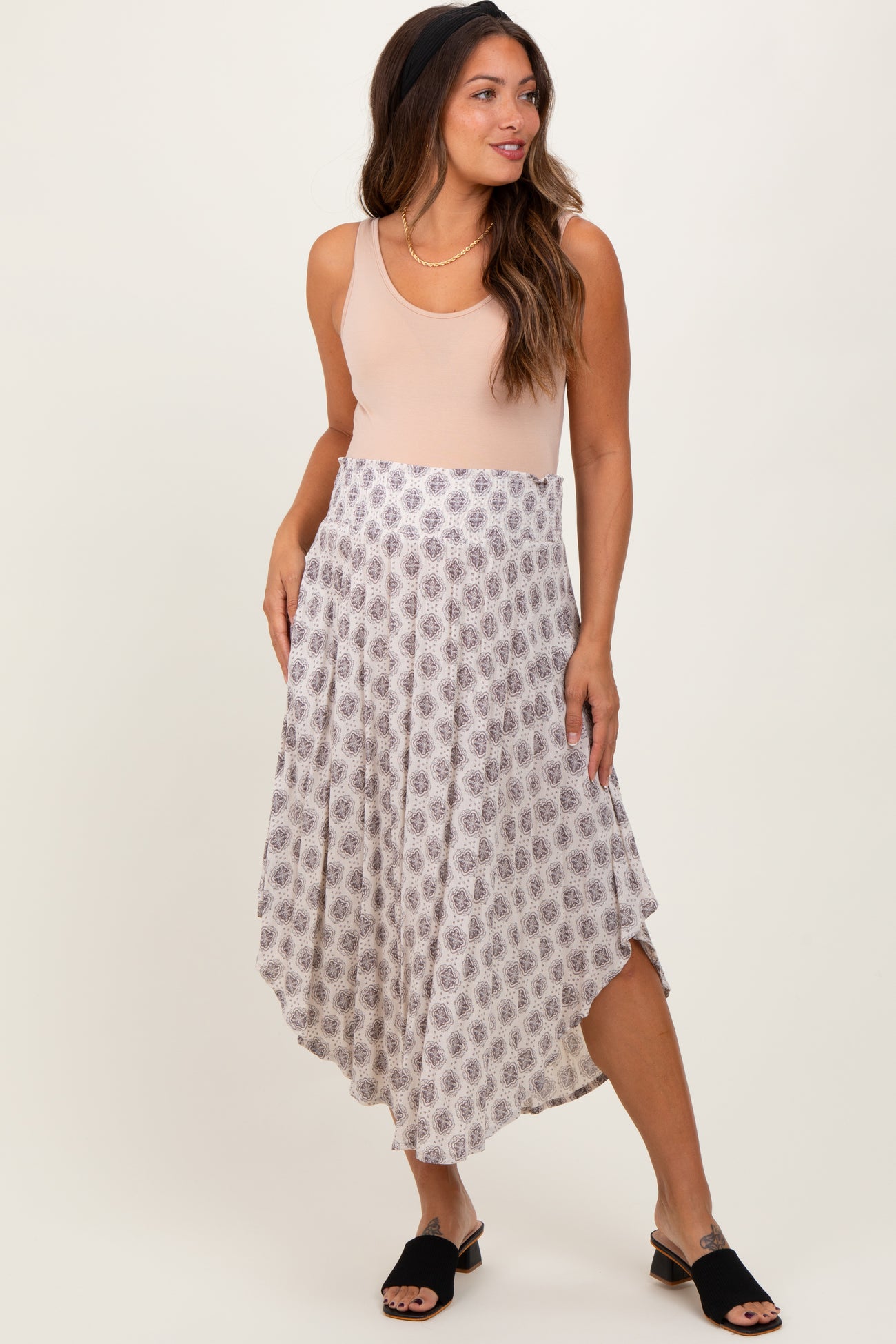 woman wearing a blush sleeveless top and a patterned maternity maxi skirt, styled with black slip-on shoes
