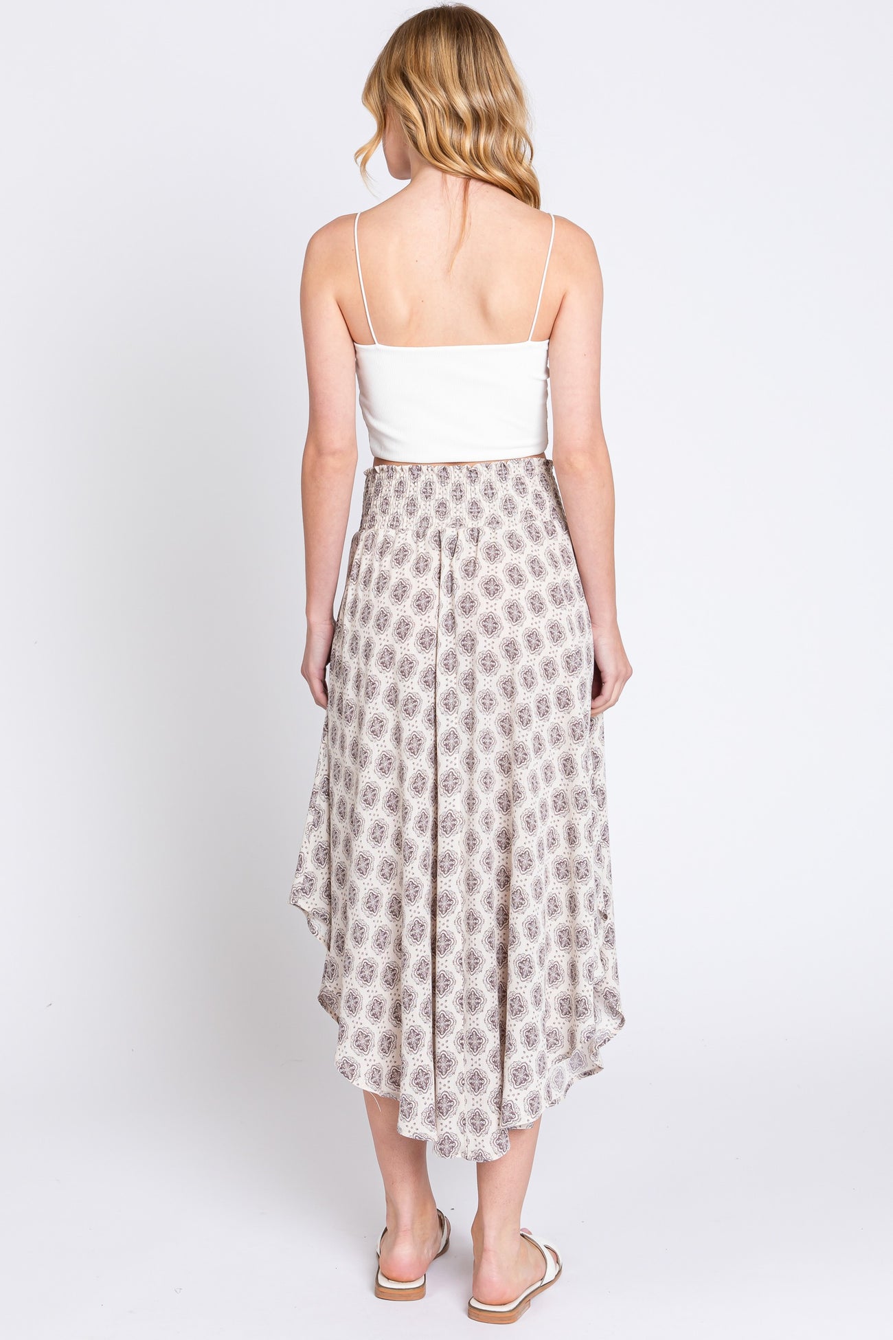 woman wearing a white fitted crop top and a flowy patterned midi skirt with a high-low hem