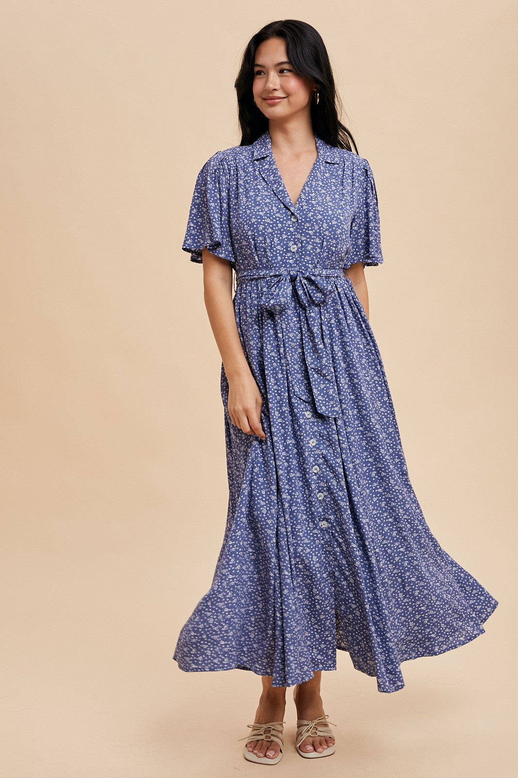 woman wearing a blue floral maxi dress with short sleeves, button details, and a tie waist