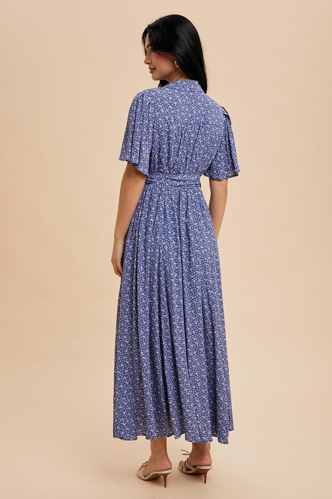 woman wearing a back view of a blue floral maxi dress with flutter sleeves and a cinched waist