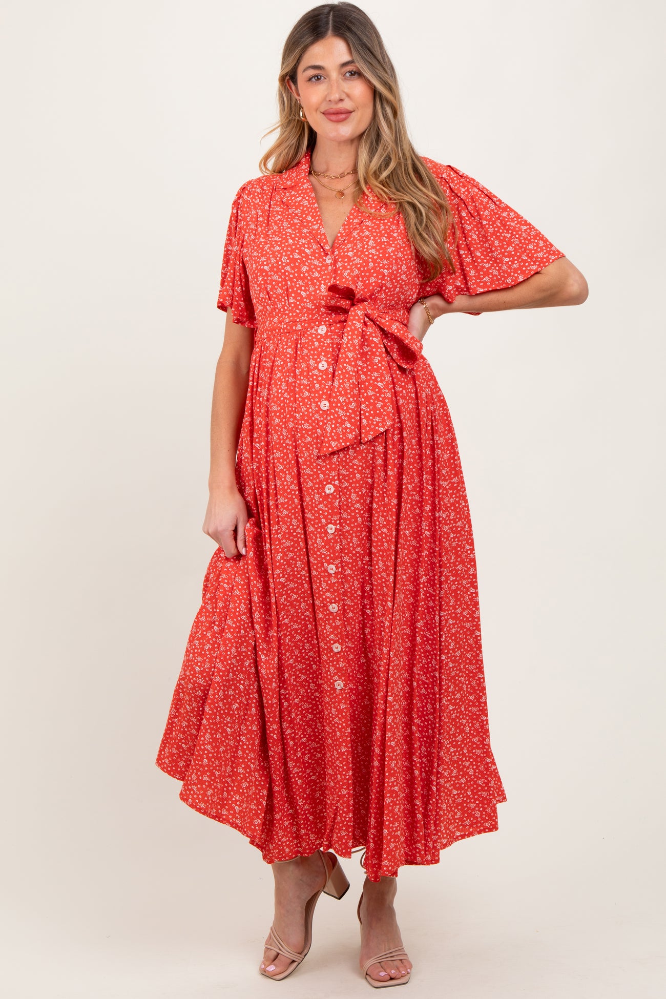 woman wearing a red floral maternity dress with short sleeves, button-down front, and tie detail at the waist