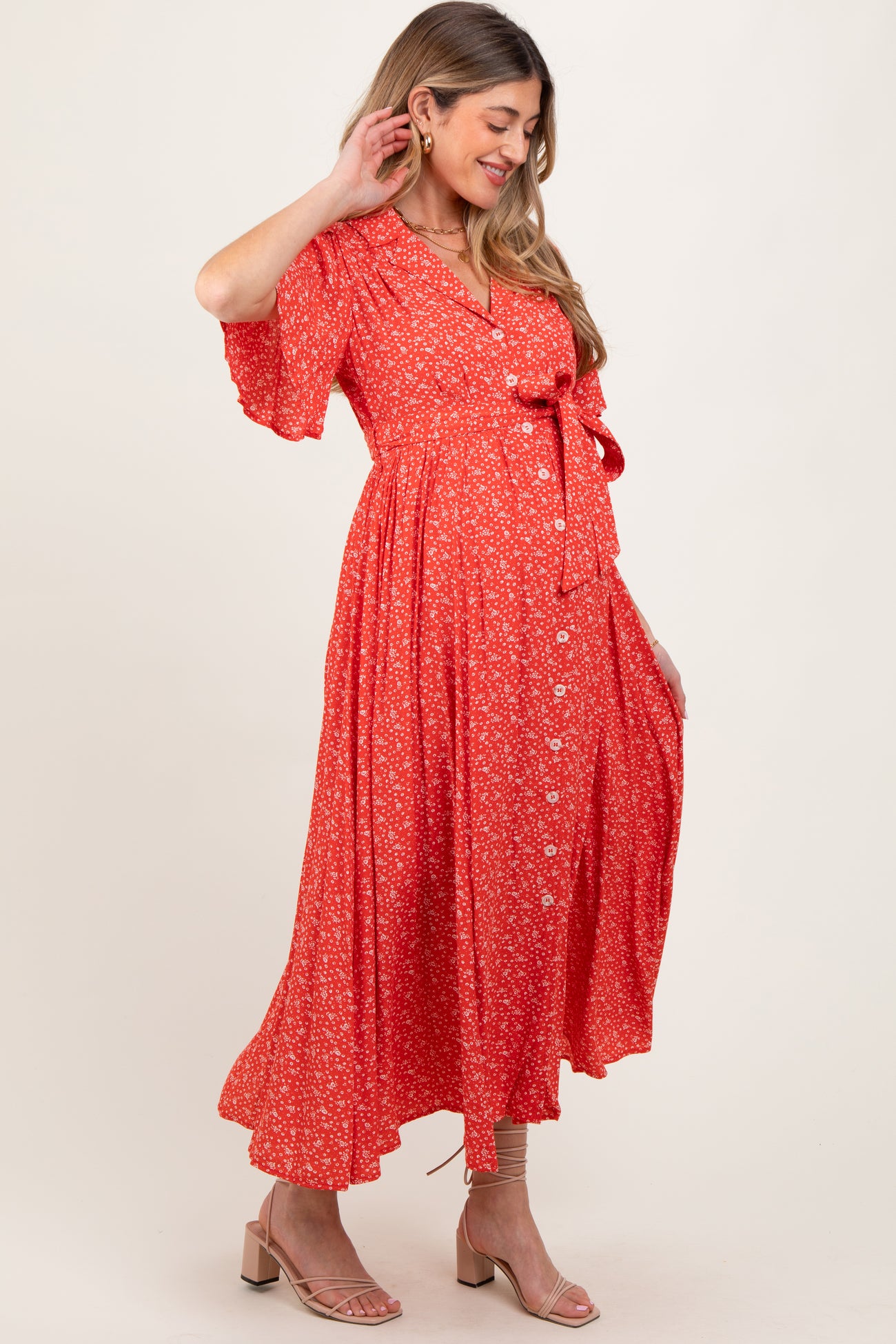 woman wearing a red floral maternity maxi dress with a tie waist and button details, showcasing her baby bump