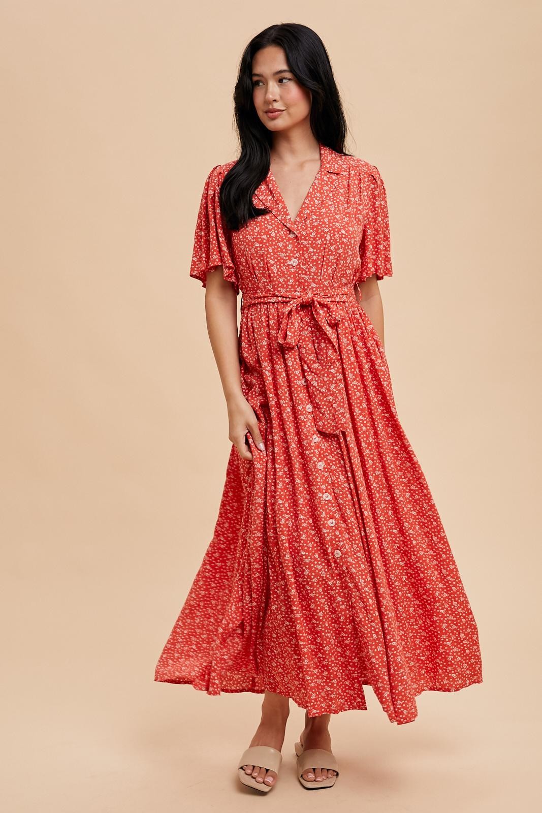 woman wearing a red floral maxi dress with short sleeves and a tie waist, standing against a neutral background