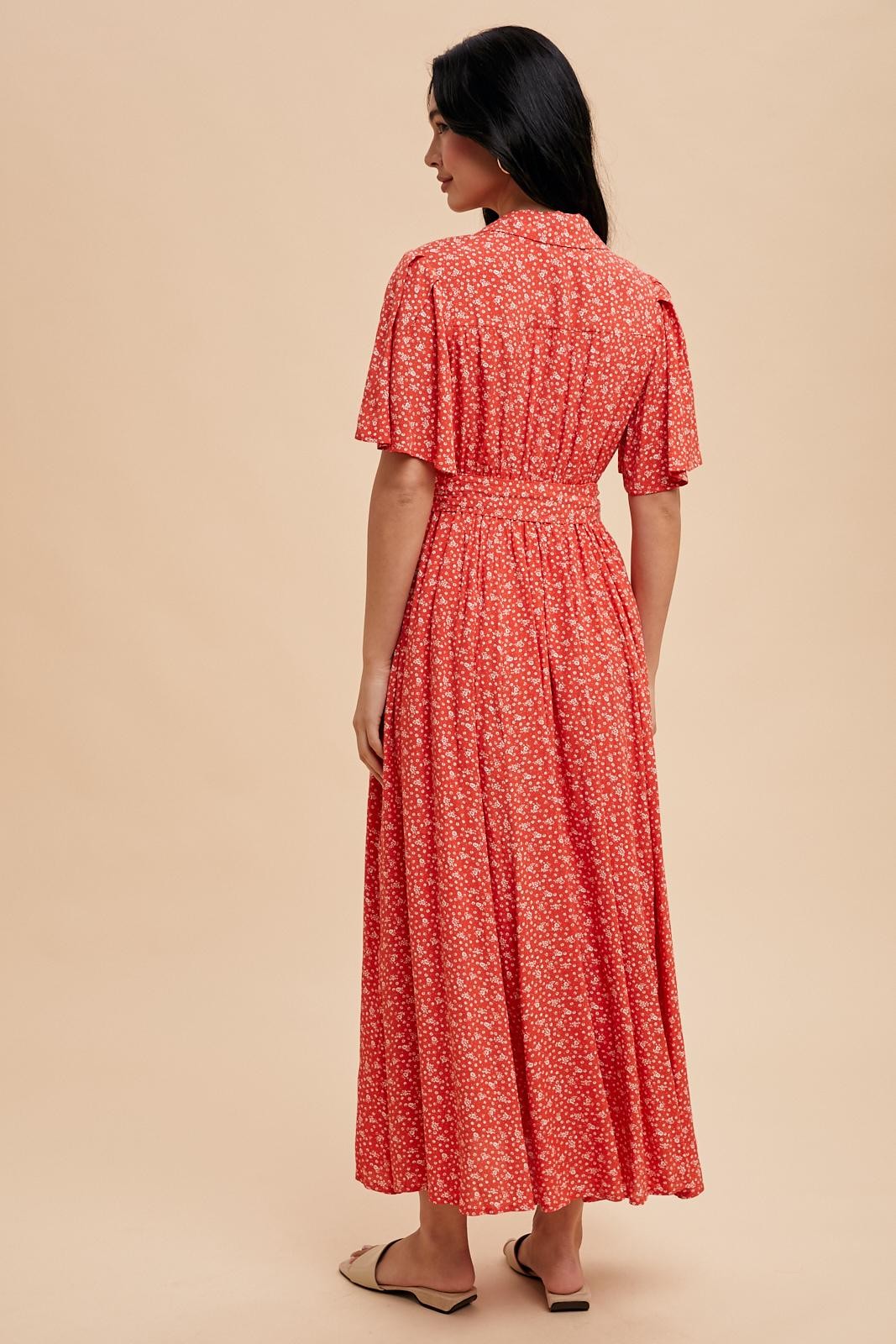 woman wearing a red floral maxi dress with short sleeves, seen from the back against a beige background