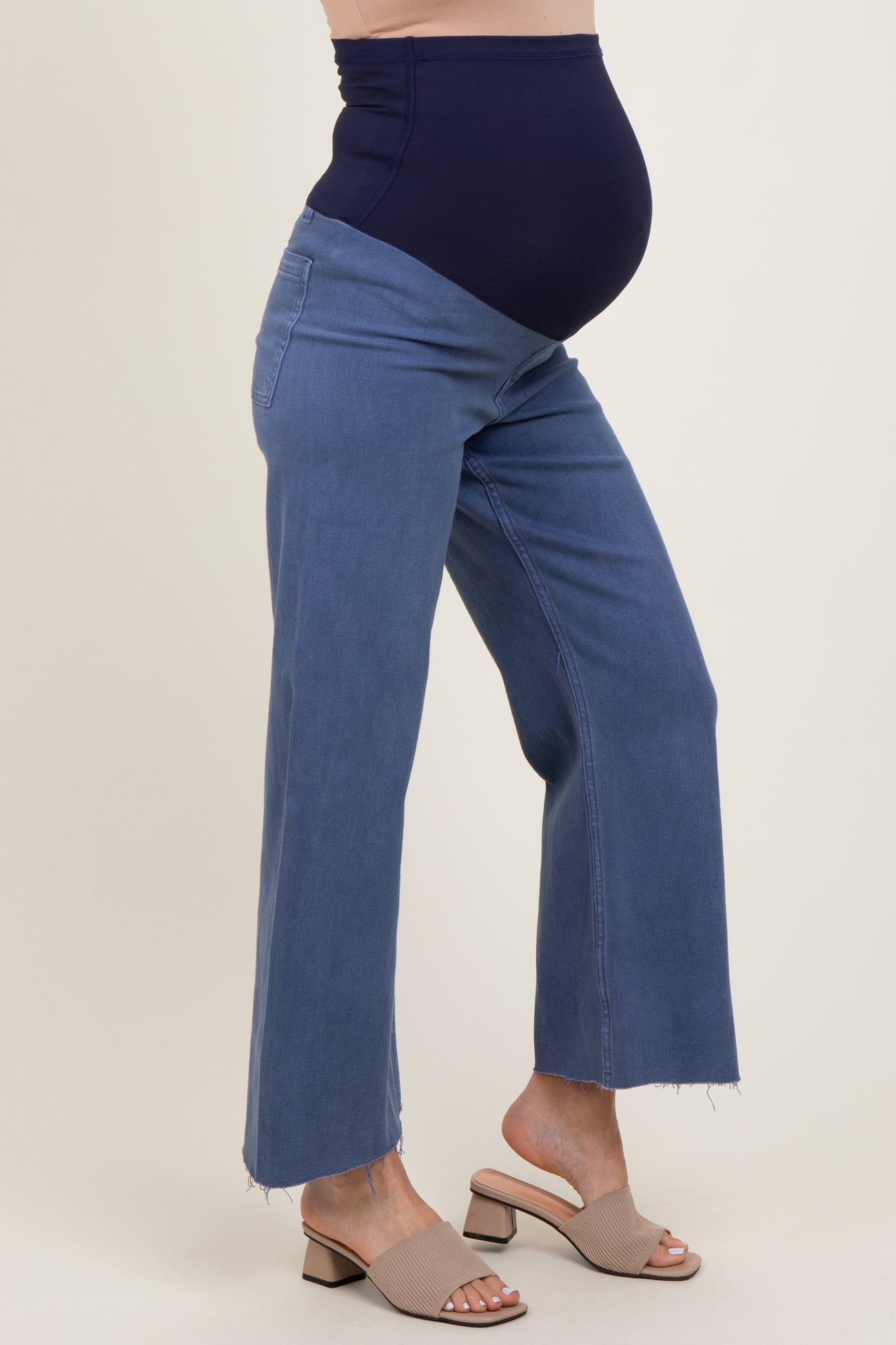 woman wearing a pair of light blue maternity jeans with a dark blue over-the-bump panel, showcasing her baby bump