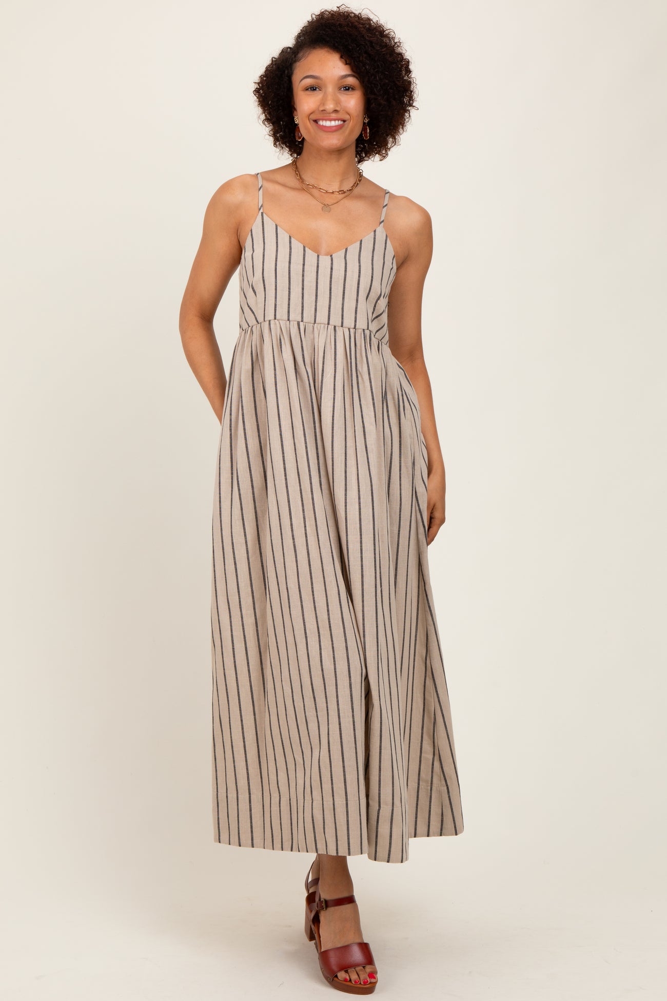 woman wearing a beige striped maxi dress with thin straps and a flared skirt, styled with red heeled sandals
