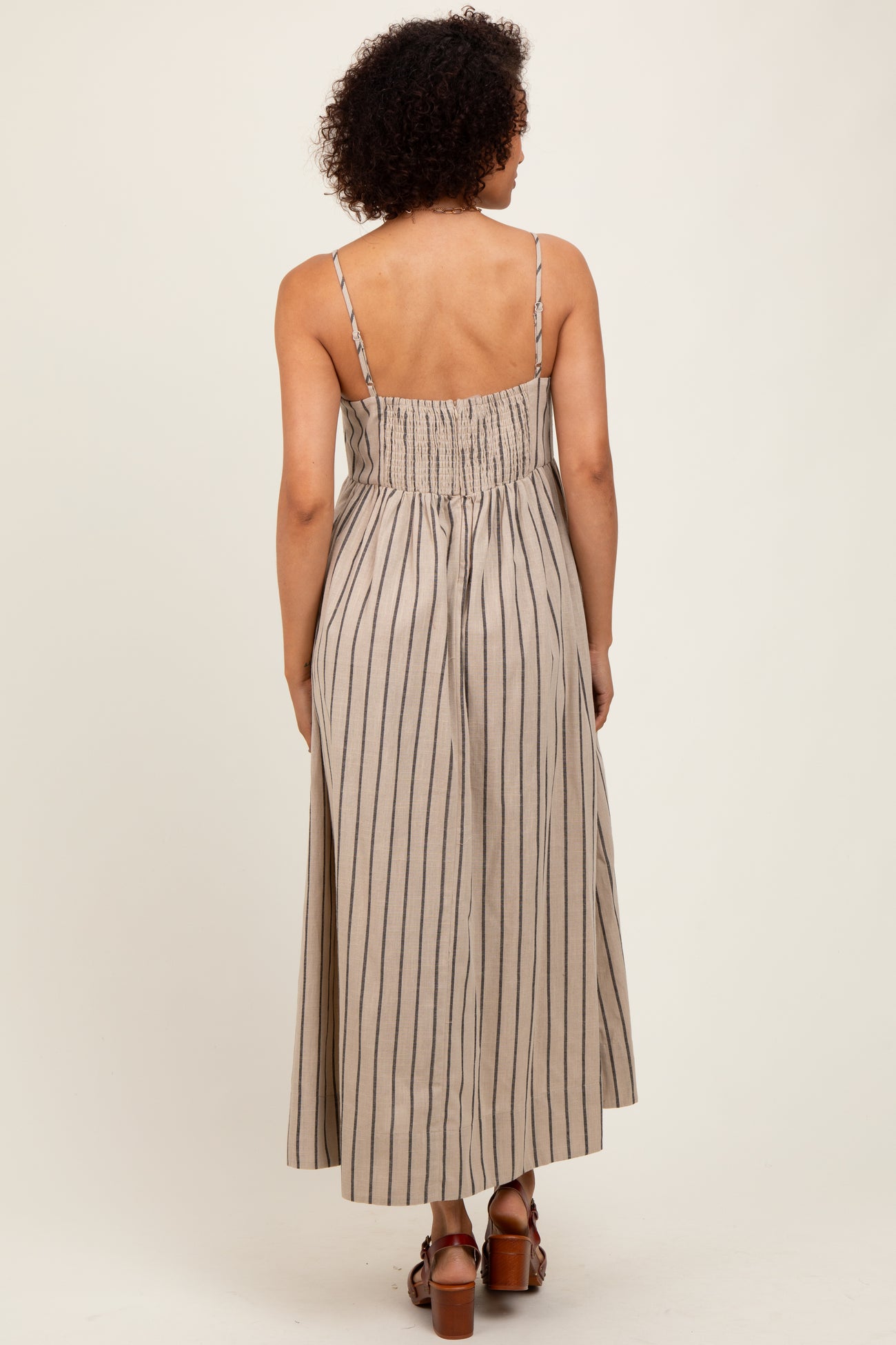 woman wearing a back view of a light brown striped maxi dress with spaghetti straps and a smocked bodice