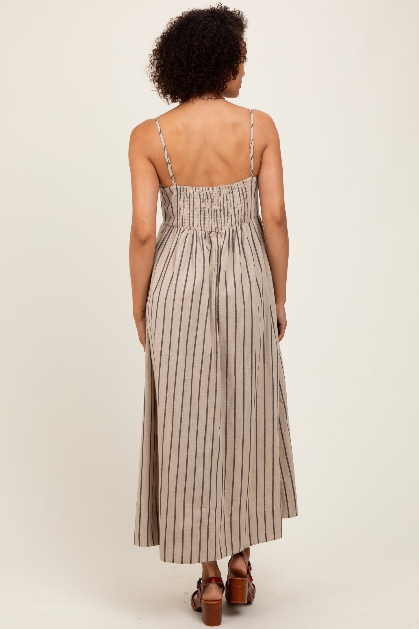 woman wearing a back view of a light brown striped maxi dress with spaghetti straps and a smocked bodice