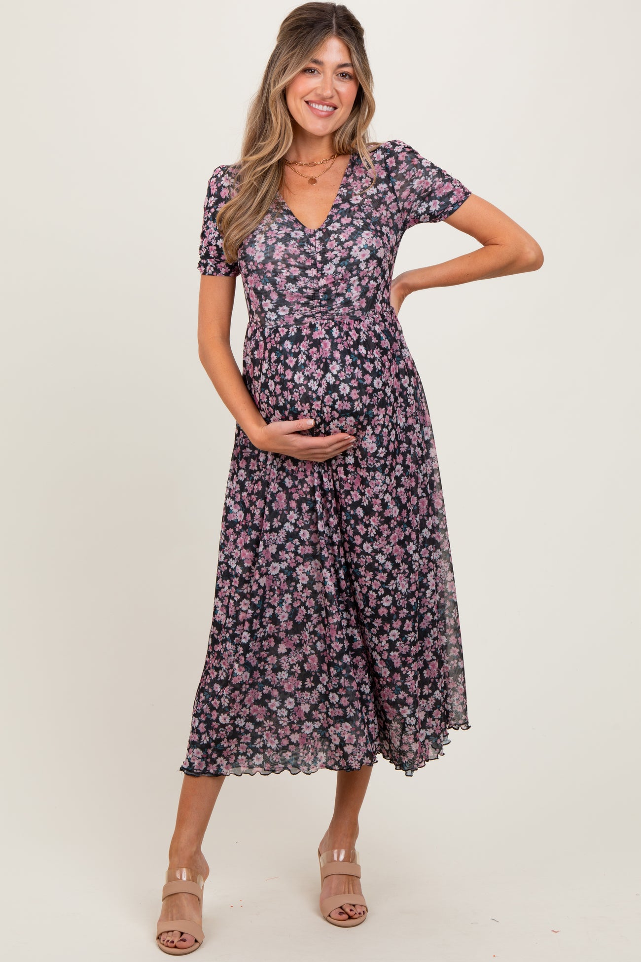 woman wearing a black floral maternity dress with short sleeves and a flowing skirt, cradling her baby bump