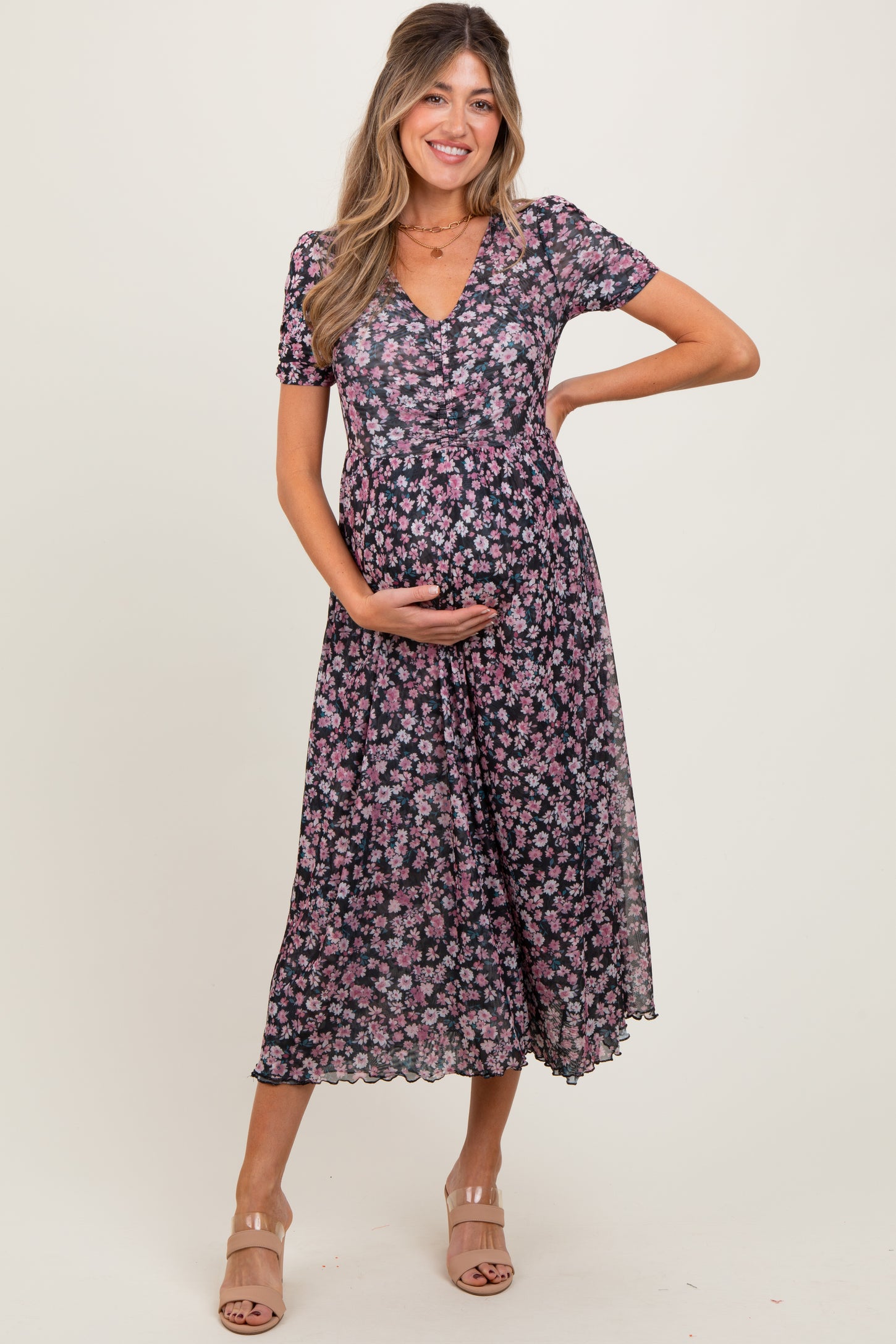woman wearing a black floral maternity dress with short sleeves and a flowing skirt, cradling her baby bump