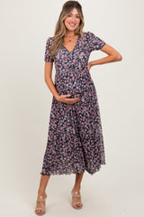 woman wearing a black floral maternity dress with short sleeves and a flowing skirt, cradling her baby bump