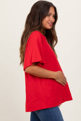 woman wearing a bright red oversized maternity top and holding her baby bump, paired with blue jeans