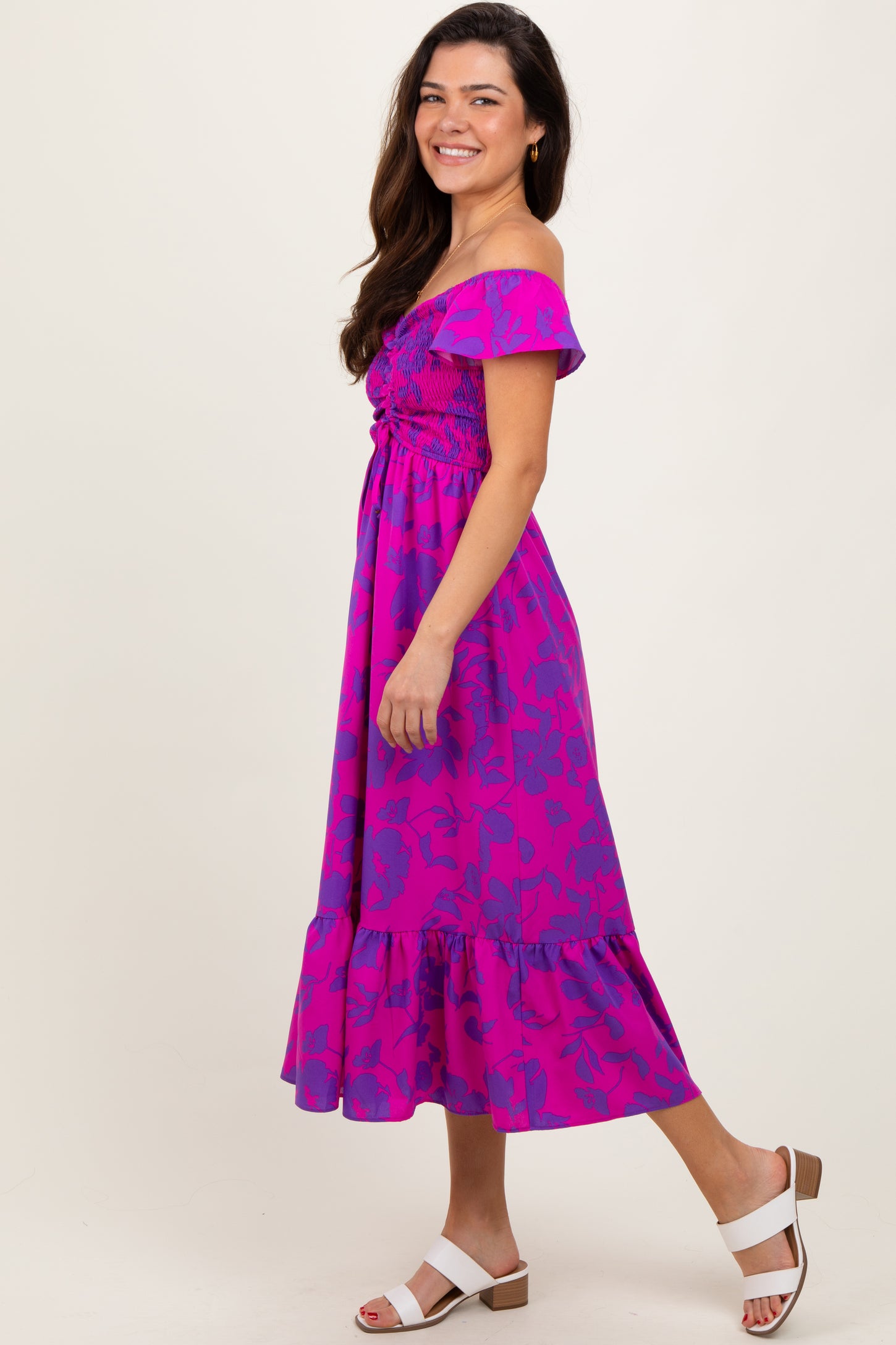 woman wearing a bright pink off-the-shoulder floral midi dress with a ruffled hem and white block-heel sandals