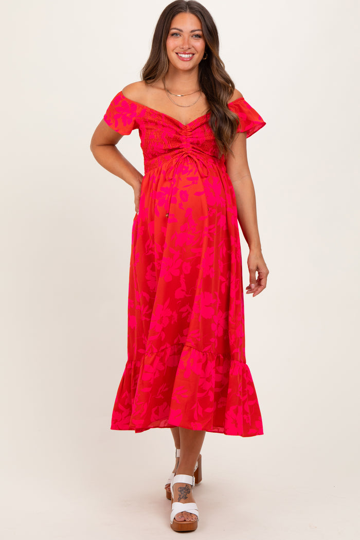 woman wearing a bright pink floral off-shoulder maternity dress with ruching and a ruffled hem, displaying her baby bump