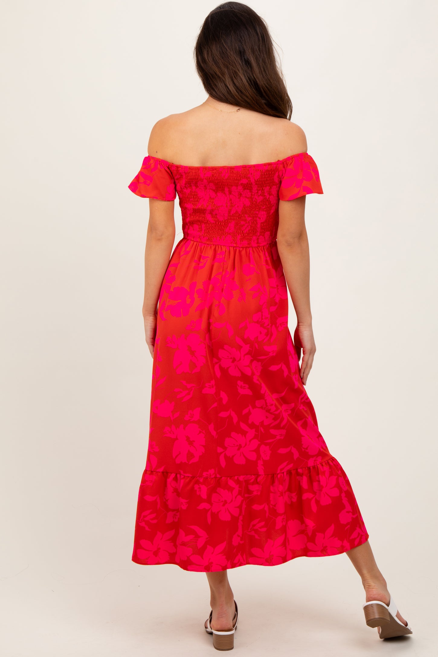 woman wearing a vibrant pink off-the-shoulder maxi dress with floral patterns and ruffle sleeves, viewed from the back