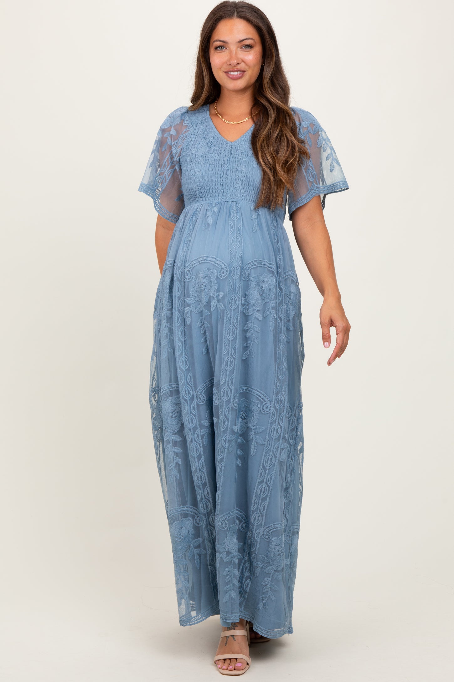 woman wearing a blue floral lace maternity maxi dress with short flutter sleeves and a visible baby bump