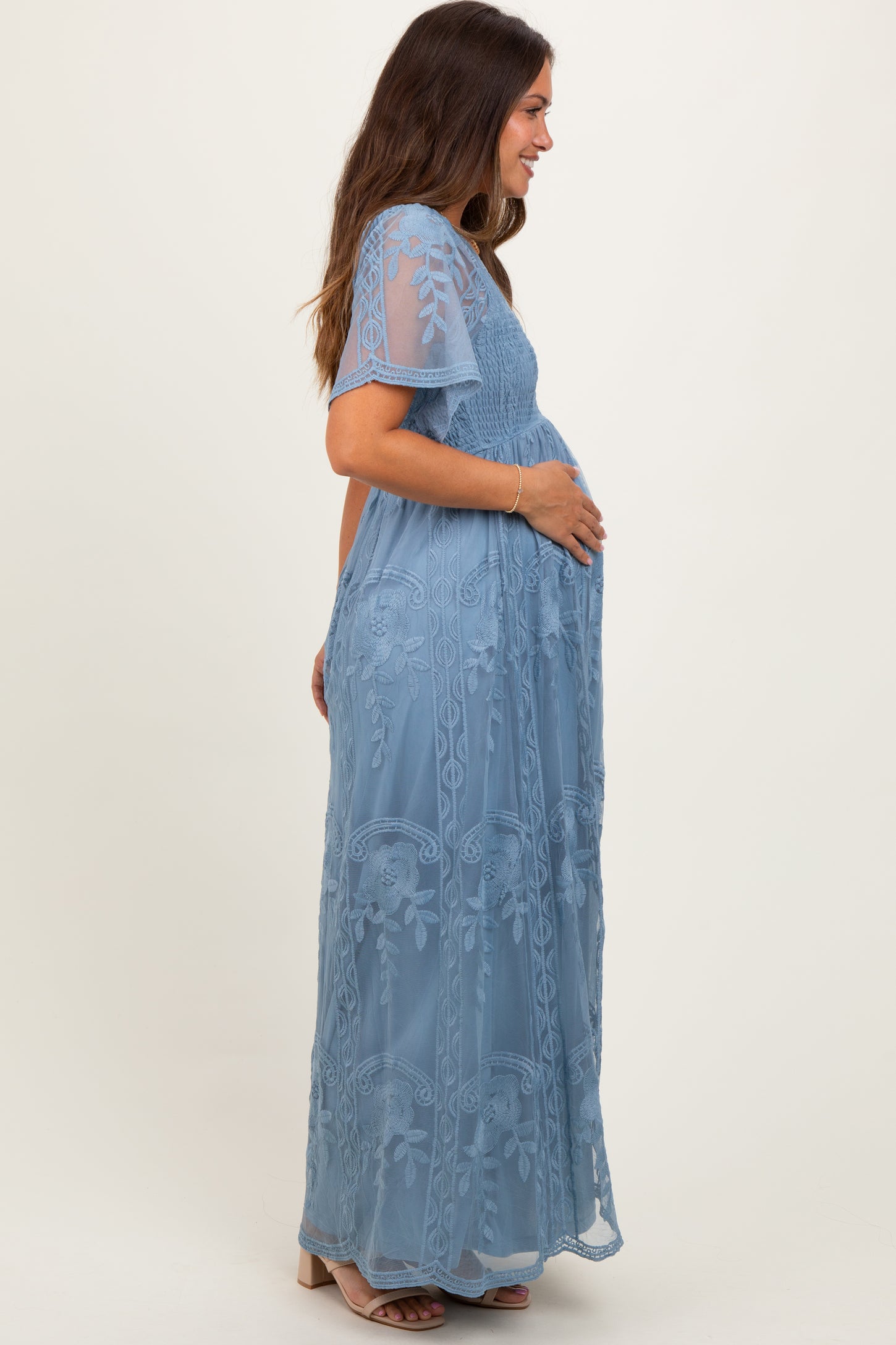woman wearing a light blue maternity maxi dress with floral embroidery and short sleeves, showing her baby bump
