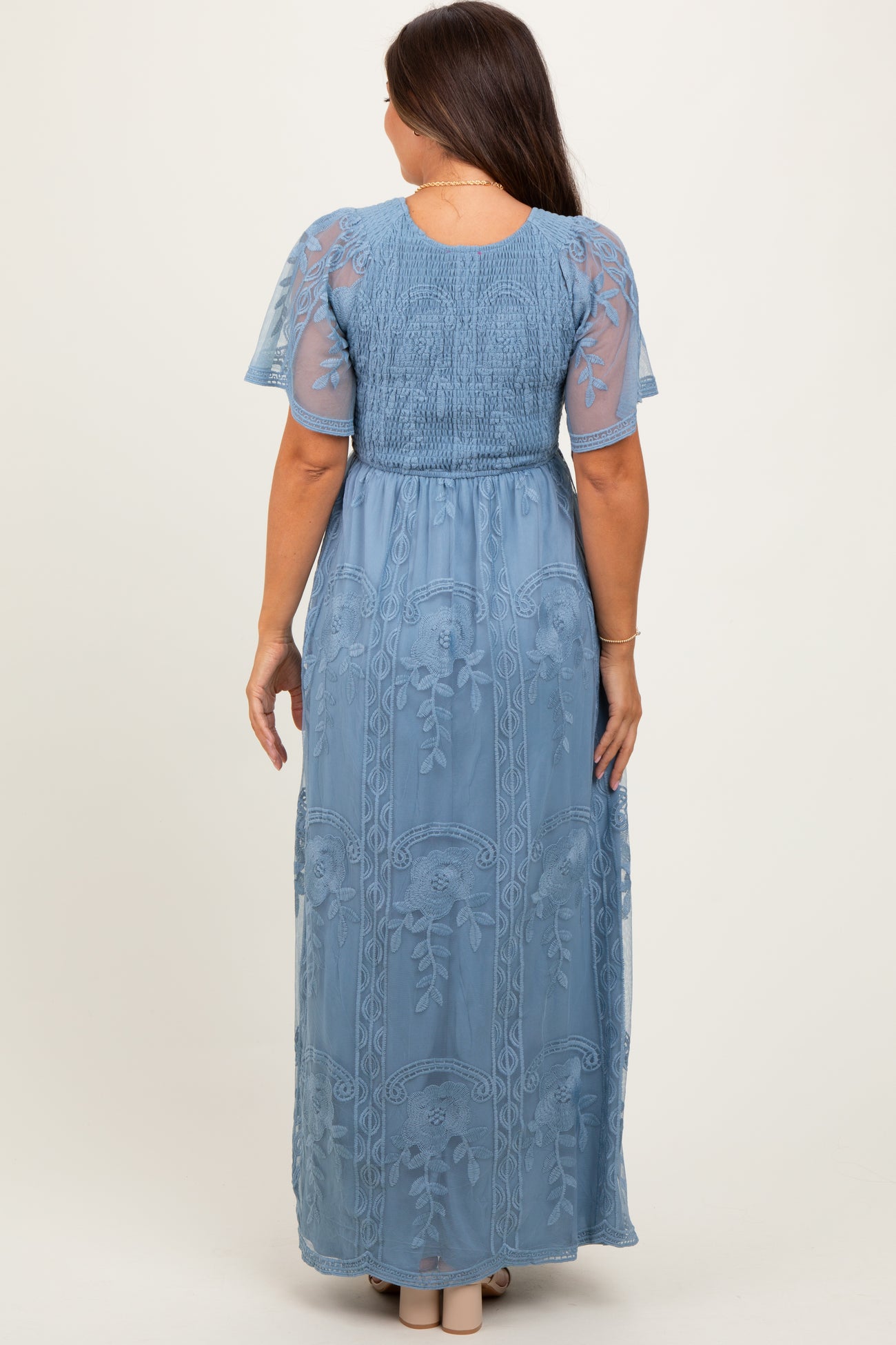 woman wearing a slate blue maxi maternity dress with short sheer sleeves and embroidered floral details