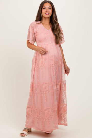 woman wearing a light pink maternity maxi dress with floral embroidery and short flutter sleeves, showcasing her baby bump