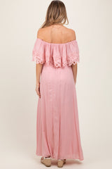 woman wearing a pink off-the-shoulder maternity maxi dress with lace detailing on the sleeves, showing a baby bump from the back