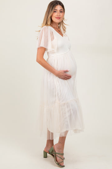 woman wearing a white midi maternity dress with sheer puff sleeves and a visible baby bump