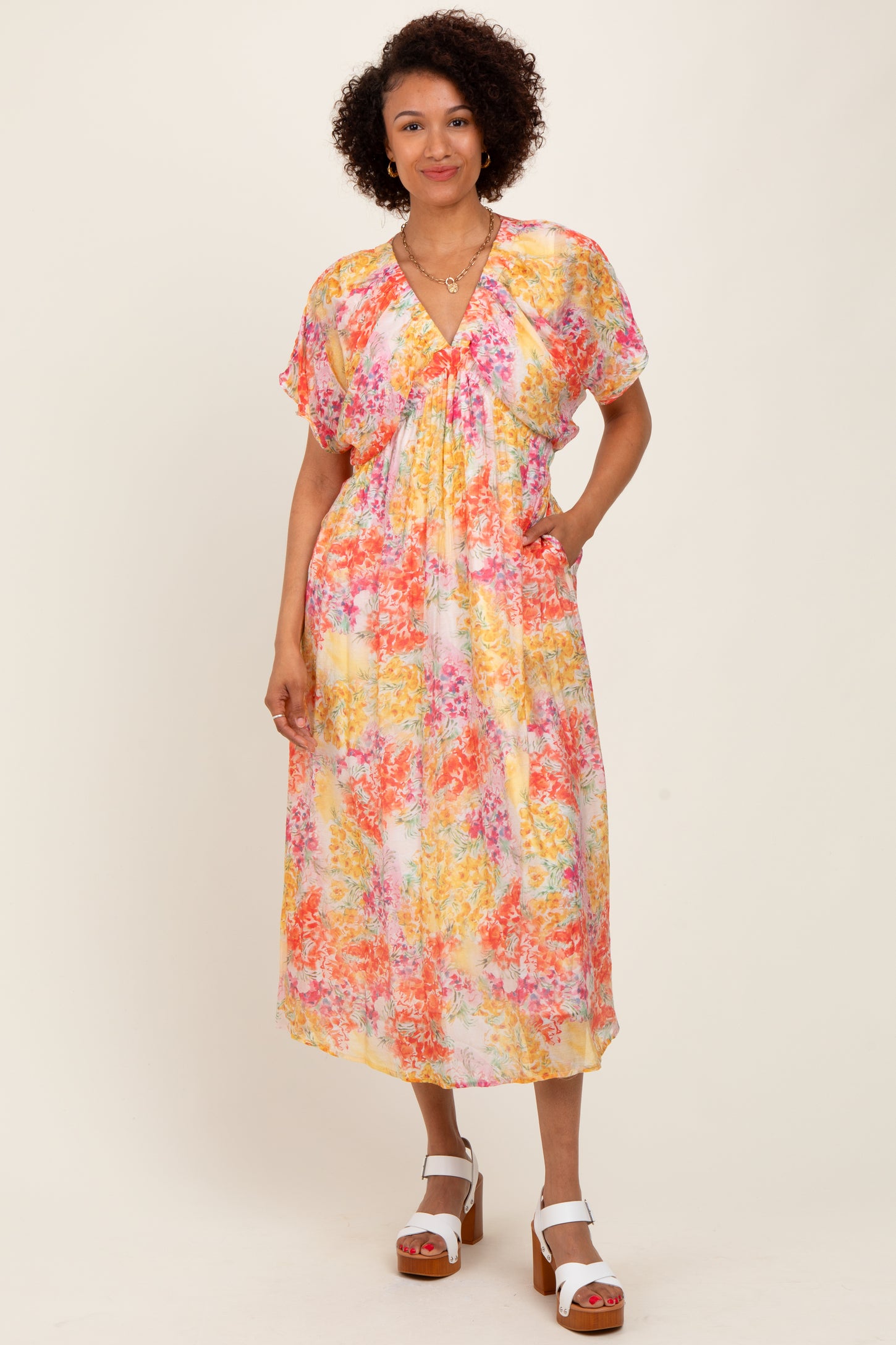 woman wearing a colorful floral midi dress with short sleeves and pockets, standing with hands in pockets