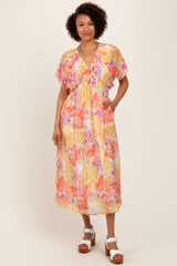 woman wearing a colorful floral midi dress with short sleeves and pockets, standing with hands in pockets