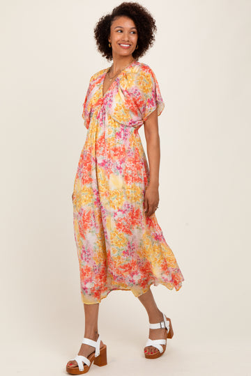 woman wearing a floral midi dress with short flutter sleeves in shades of pink, yellow, and cream, paired with white block-heeled sandals