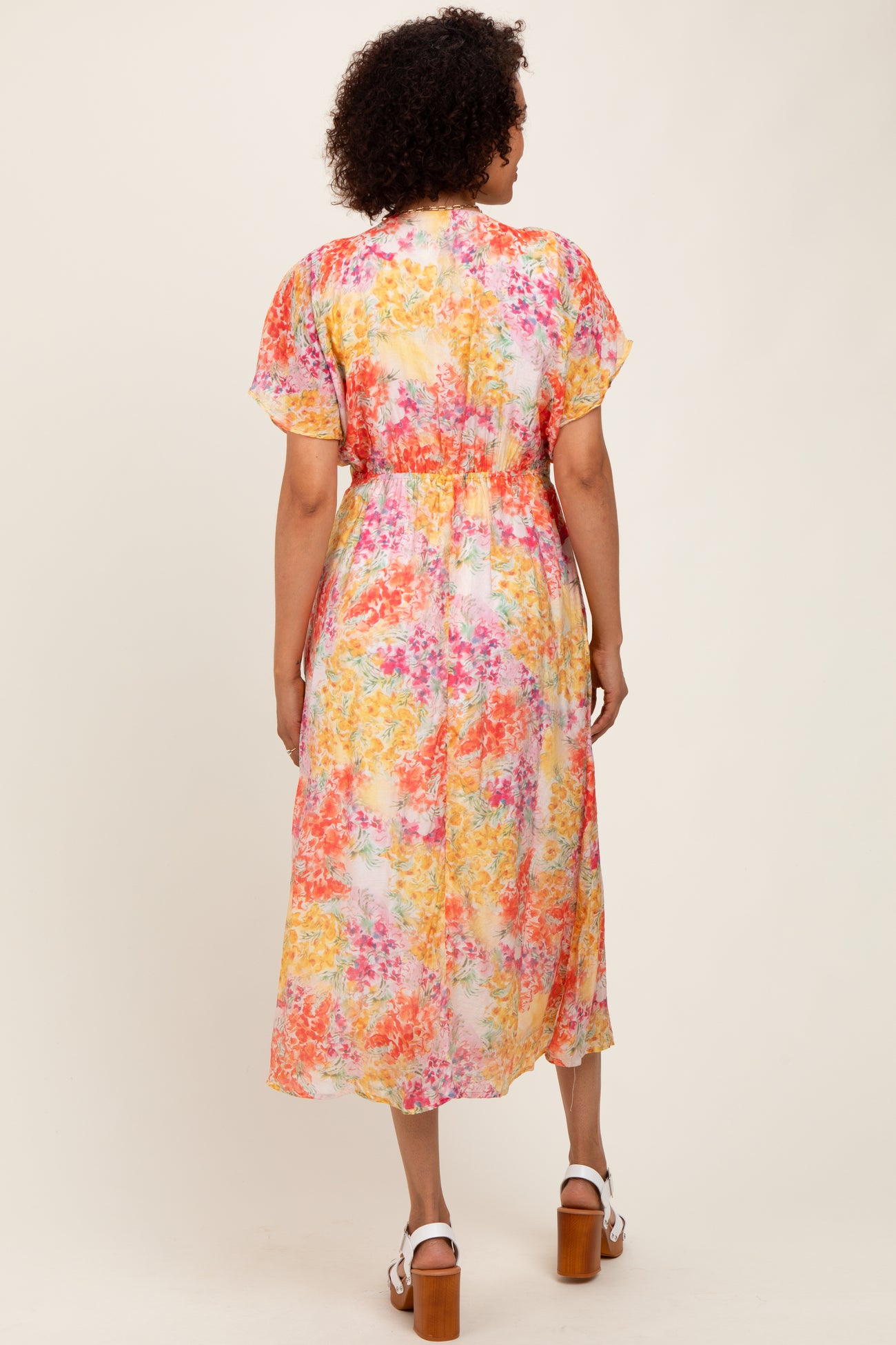 woman wearing a colorful floral midi dress with short sleeves and a cinched waist, viewed from the back