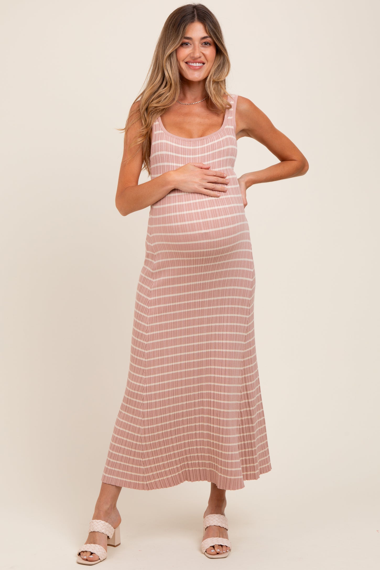 woman wearing a pink and white striped maternity maxi dress and holding her baby bump