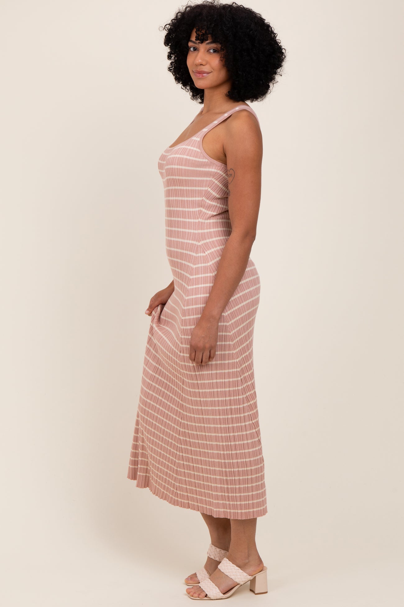 woman wearing a pink and white striped midi dress with thin straps and a flowy skirt, standing sideways