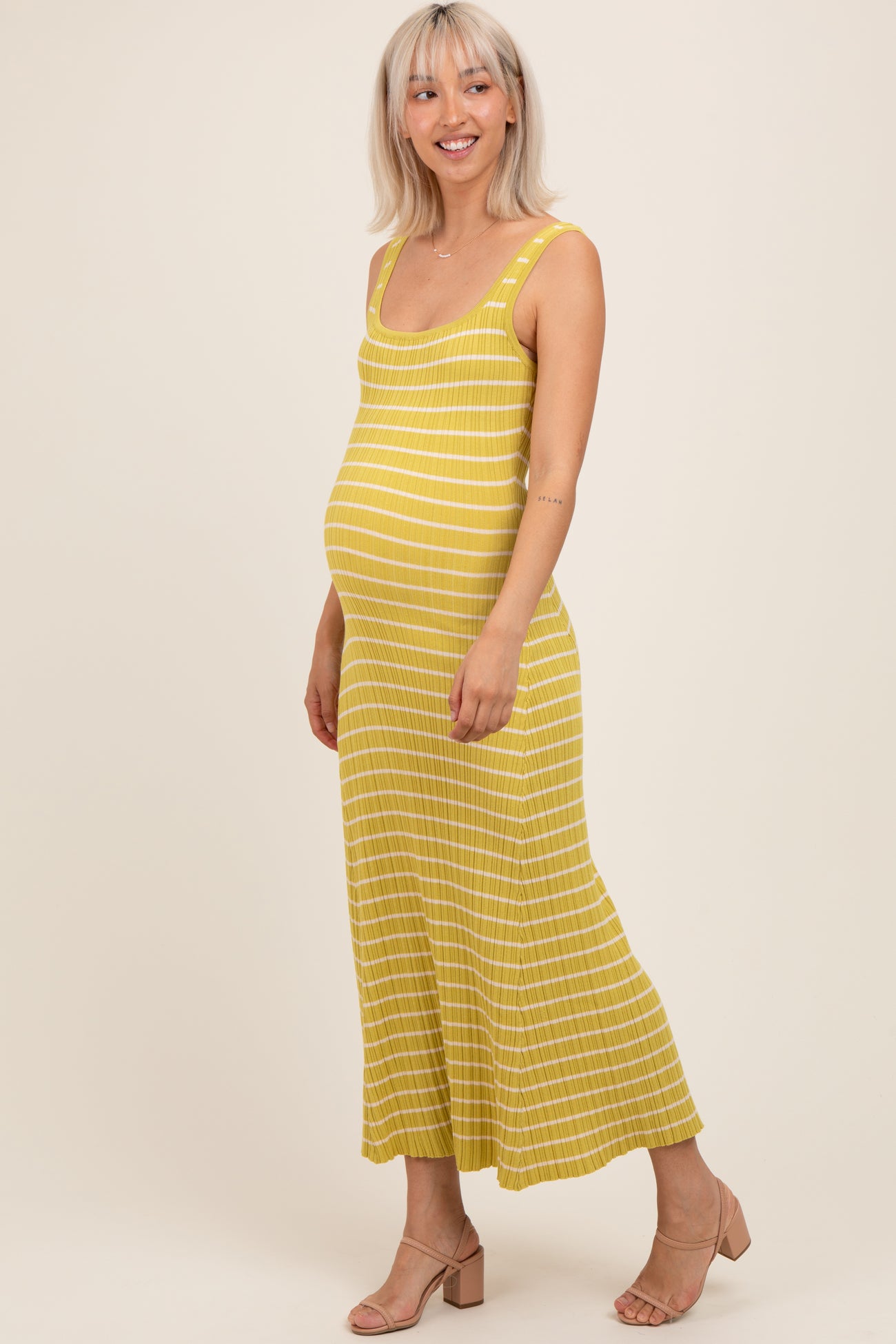 woman wearing a yellow striped maternity dress, showcasing her baby bump, standing against a neutral background